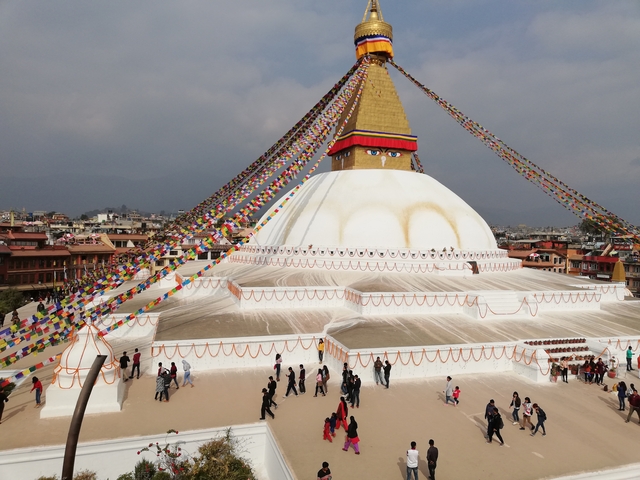 Boudhanath Stupa with prayer flags and people around the base.