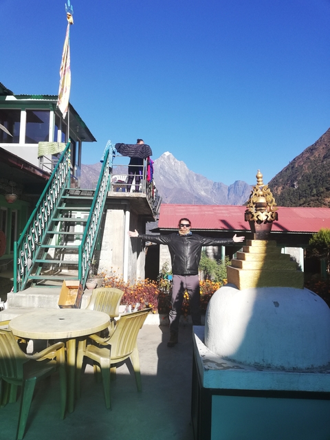 Person posing with mountains in the background under a clear blue sky.