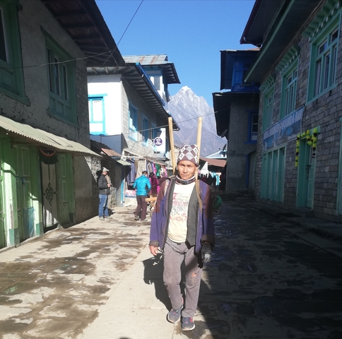 People walking through a narrow street with shops and mountains in the background.