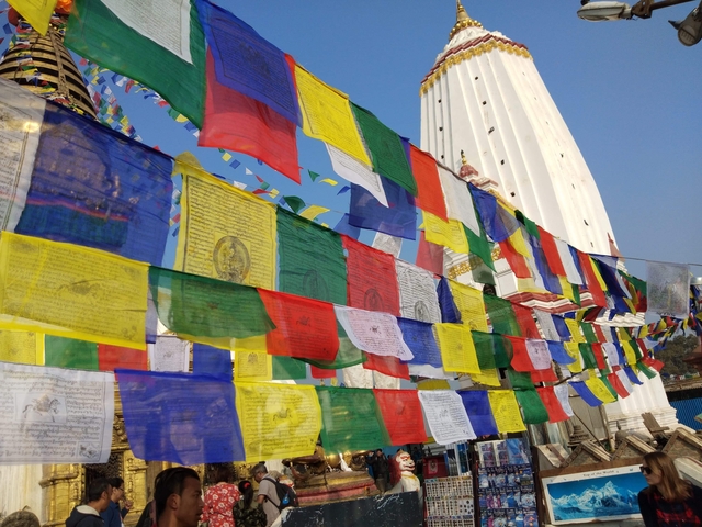 Colorful prayer flags waving in front of a white stupa under a clear sky.