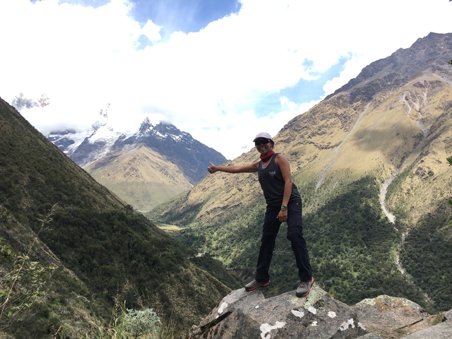 Person standing on a mountain trail with snow-capped peaks.