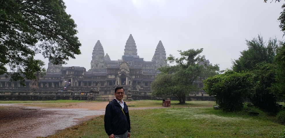 A visitor at Angkor Wat surrounded by lush greenery.