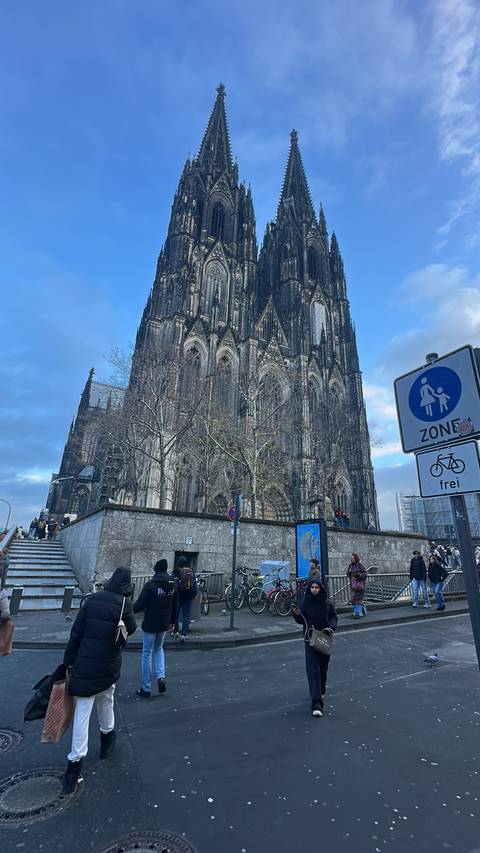 Facade of a large Gothic cathedral with pedestrians in front.