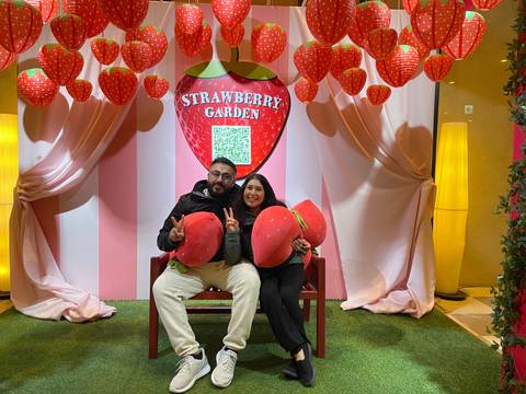       Couple holding large strawberry props in a themed garden.
  