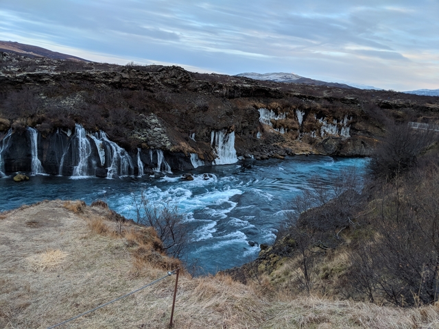      Hraunfossar waterfall in Iceland with icy edges and a flowing river.
  