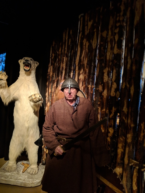       Man in Viking attire with a polar bear display, inside a museum or exhibit.
  