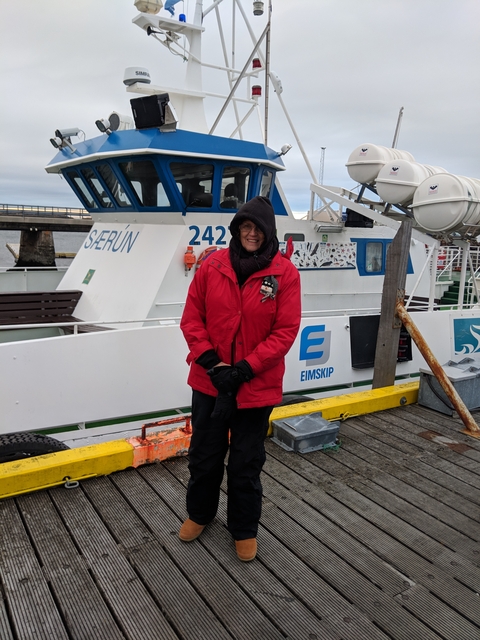       Person in red jacket posing on a dock next to a fishing boat.
  