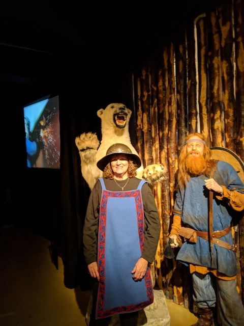       Person dressed in Viking clothing with a polar bear display, inside a museum or exhibit.
  