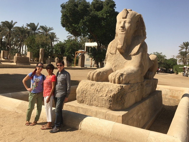 People posing with a large sphinx statue in an outdoor setting.