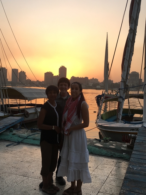 Three people posing on a boat with a sunset city skyline.
