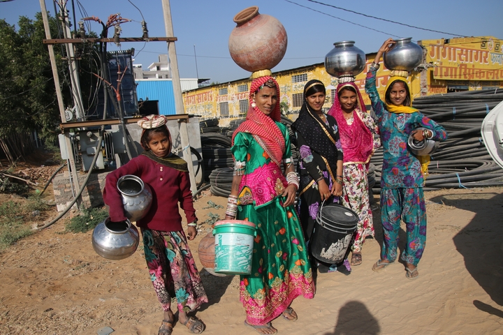 Group of women in colorful attire carrying pots on their heads.