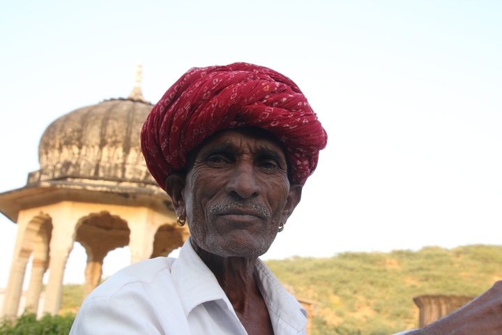 Elderly man wearing a red turban with a decorative monument in the background