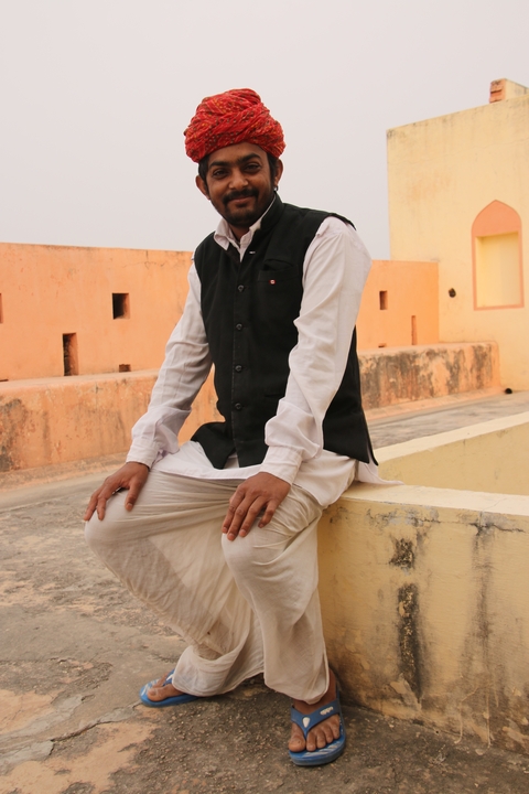 Man dressed in traditional clothing sitting on a ledge in an architectural setting.