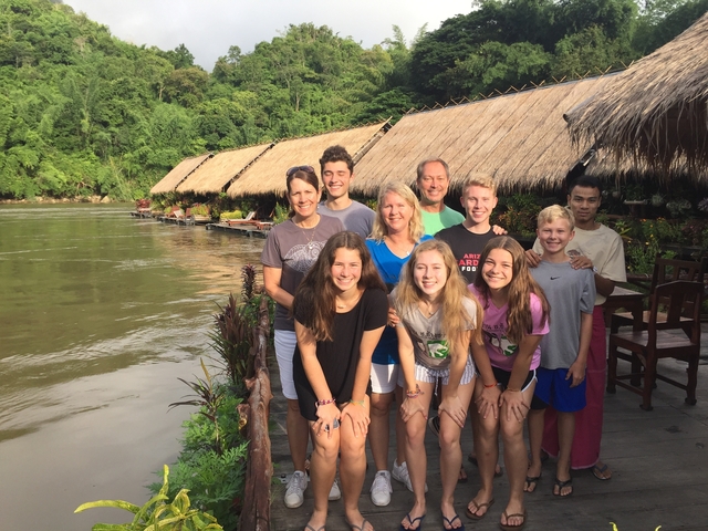 Group of people posing by a river with thatched buildings.