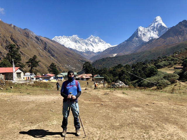       Person standing in a mountainous village with snow-capped peaks.
  