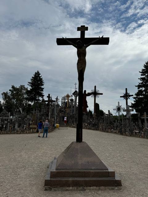 A large crucifix in a field with people walking by.