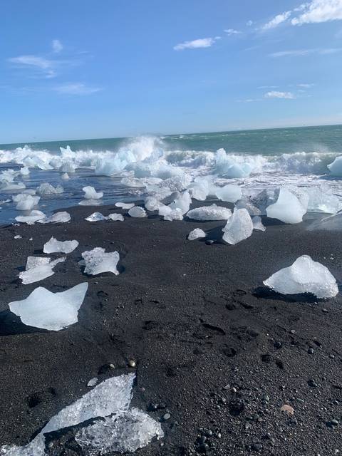 Black sand beach with ice chunks and waves.