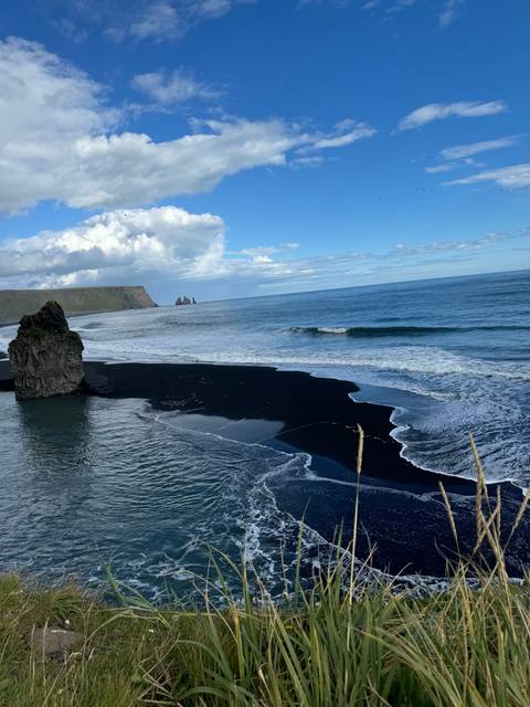Black sand beach and ocean with cliffs.