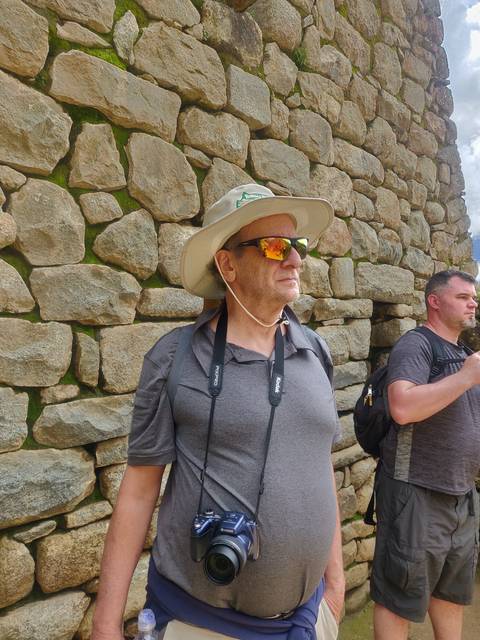 Man with hat and camera standing on stone path.