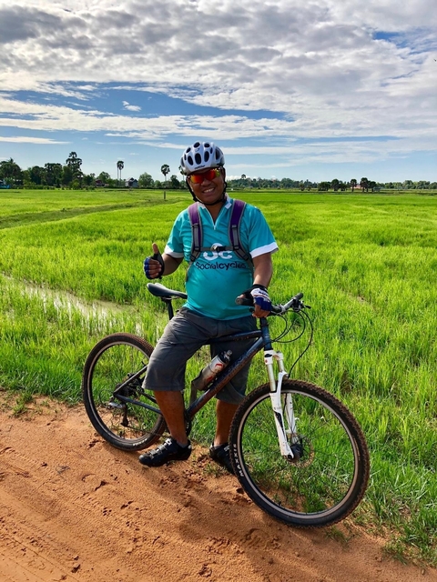 A person posing with a bicycle in a green field.