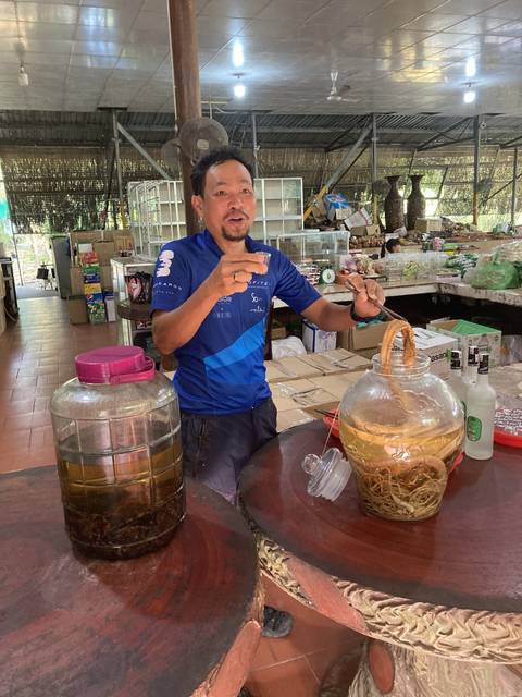A person gesturing at a food table in an indoor market setting.
