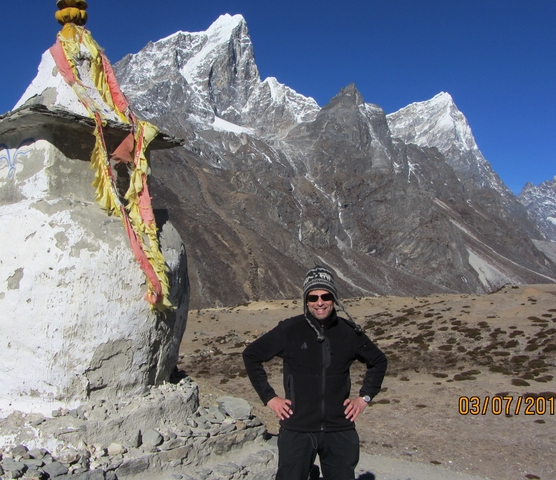       Person posing next to a chorten with mountains.
  