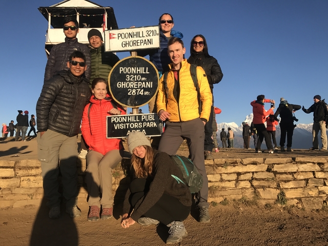 Group of hikers posing at Poon Hill viewpoint with mountain backdrop.