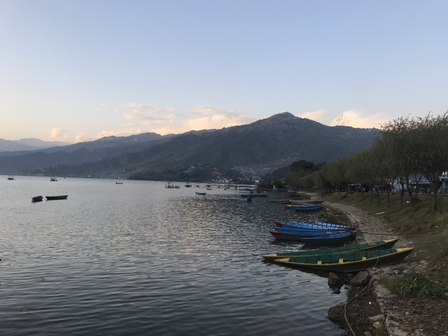       A series of boats on a calm lake with mountains in the distance.
  
