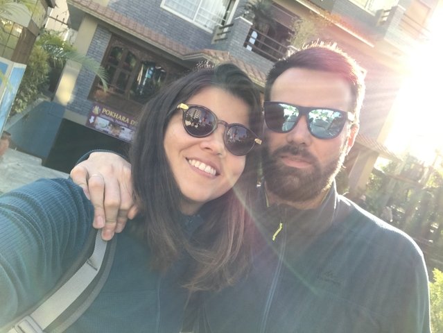       Smiling couple posing with sunglasses on in bright sunlight.
  