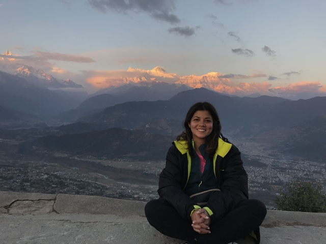       Woman sitting with a backdrop of illuminated mountains during sunset.
  