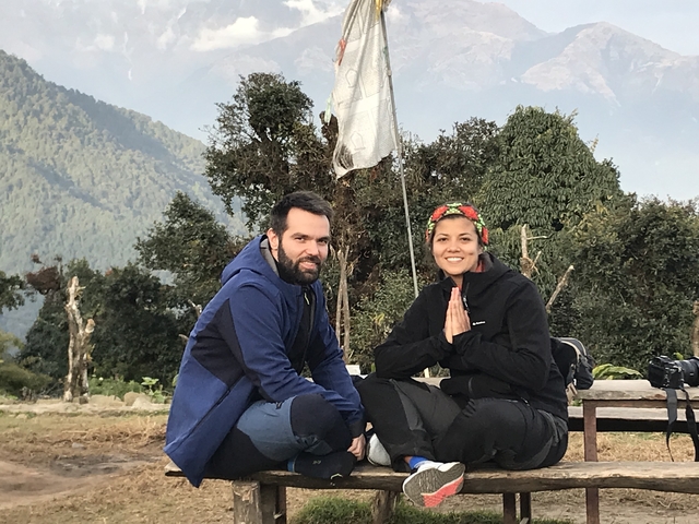       Couple sitting and meditating outdoors with mountains in the background.
  