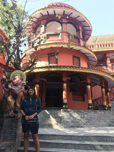       Woman standing near a red building with Ganesha statue.
  