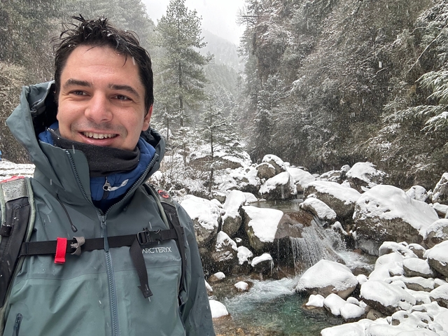 A person in a jacket smiling with a snowy landscape in the background.