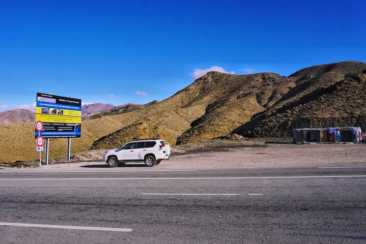       A road with a parked SUV, a sign, and brown hills in the background.
  