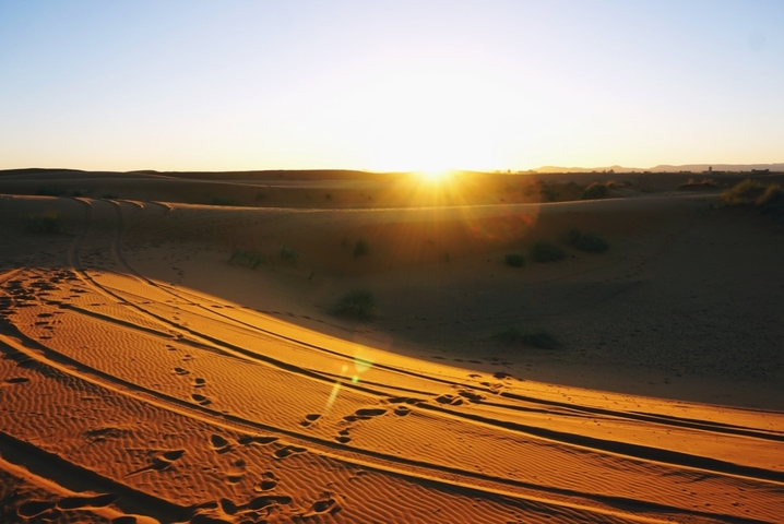 Sunrise over a desert landscape with sand dunes.