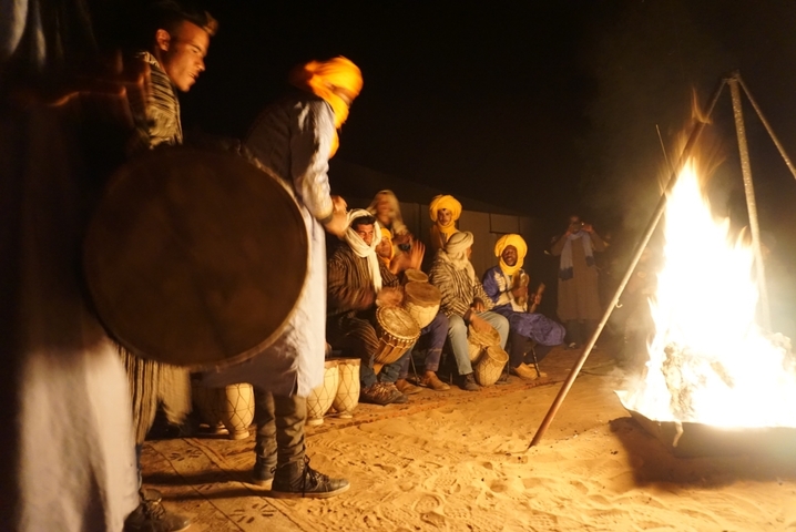 Group of people in traditional clothing around a campfire at night.