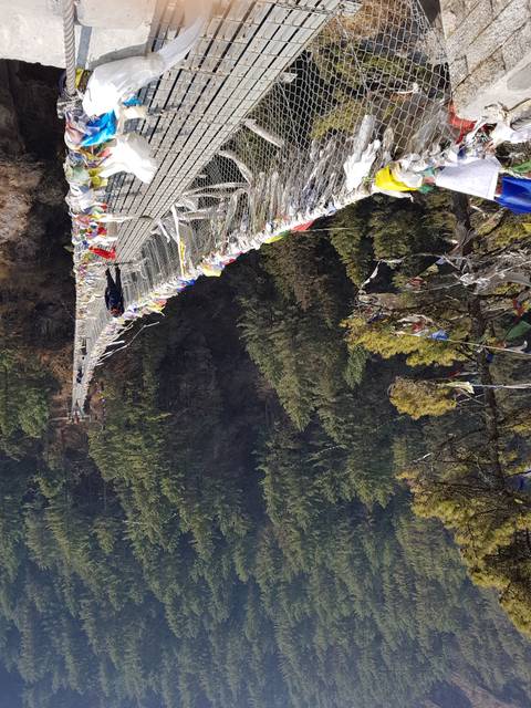 Suspension bridge with prayer flags over a forest.