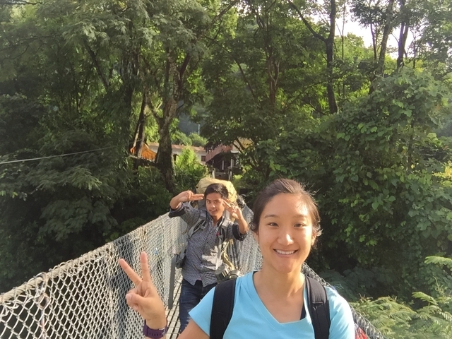 Two people posing on a suspension bridge surrounded by lush greenery.