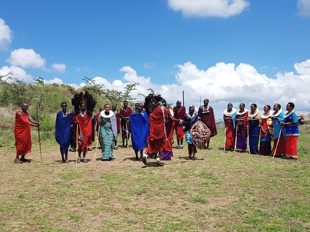 Maasai men and women standing in a field in traditional attire.
