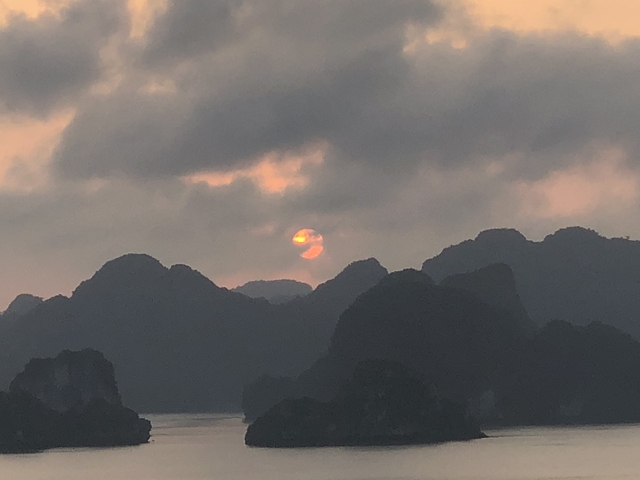 Sun setting over rugged mountains under cloudy sky.