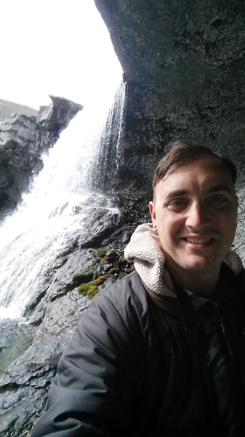 Close-up of a man smiling with a waterfall in the background.