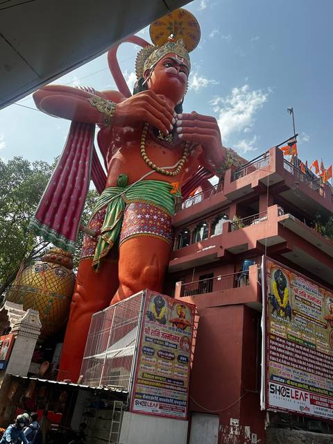 A large statue of Hanuman outside a temple with large posters.
