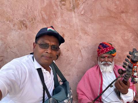 Two people, one in traditional attire, with an instrument against a textured background.