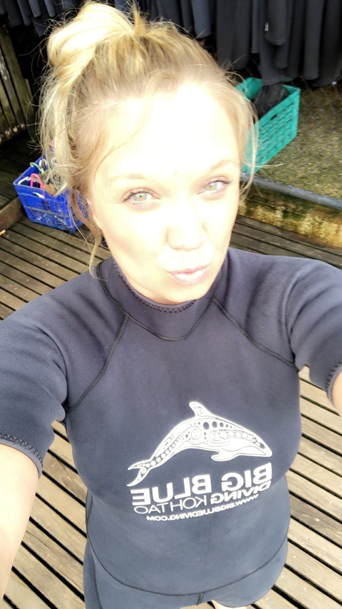 Person in a wetsuit taking a selfie with a wooden deck in the background.