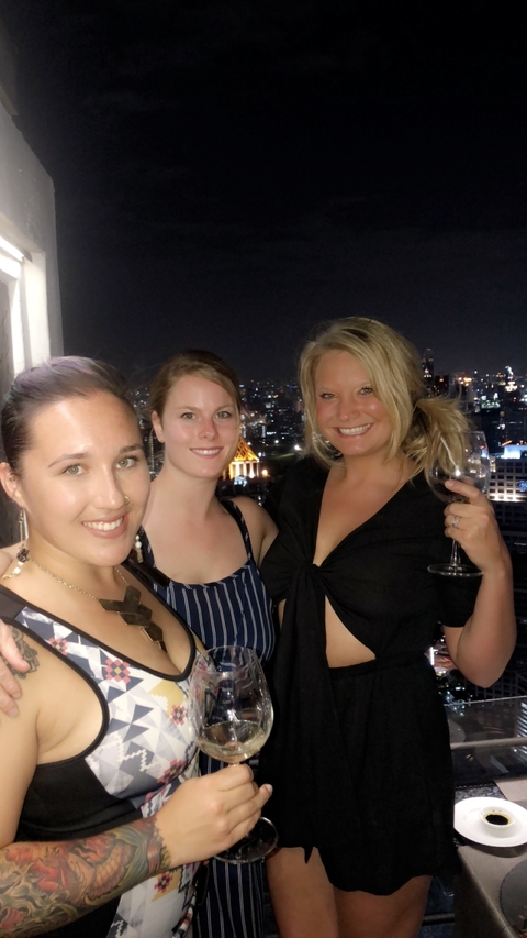 Three people smiling with a city skyline at night in the background.