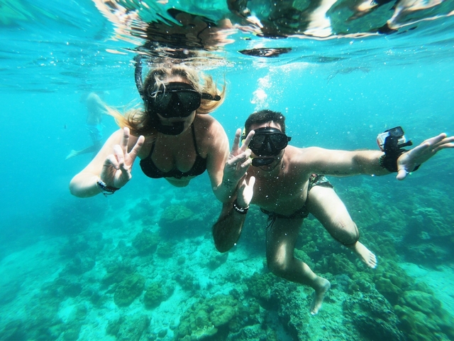 Two people snorkeling underwater, making peace signs.
