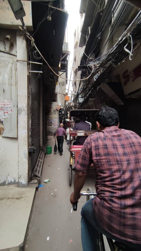 A narrow street with people riding a rickshaw surrounded by hanging wires.