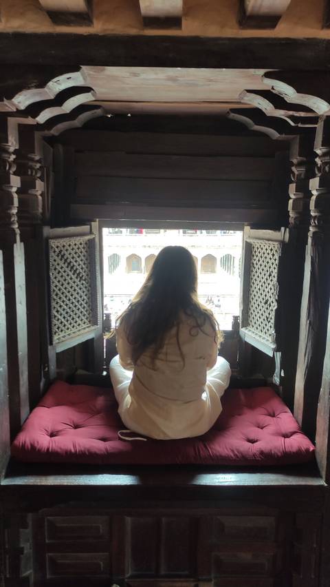 A woman sitting inside a building looking out of a window seat.