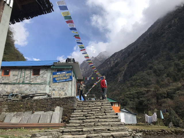 People standing near a guesthouse in the mountains with flags.