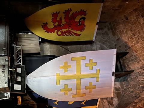 Flags with medieval emblems hanging inside a dim setting.
